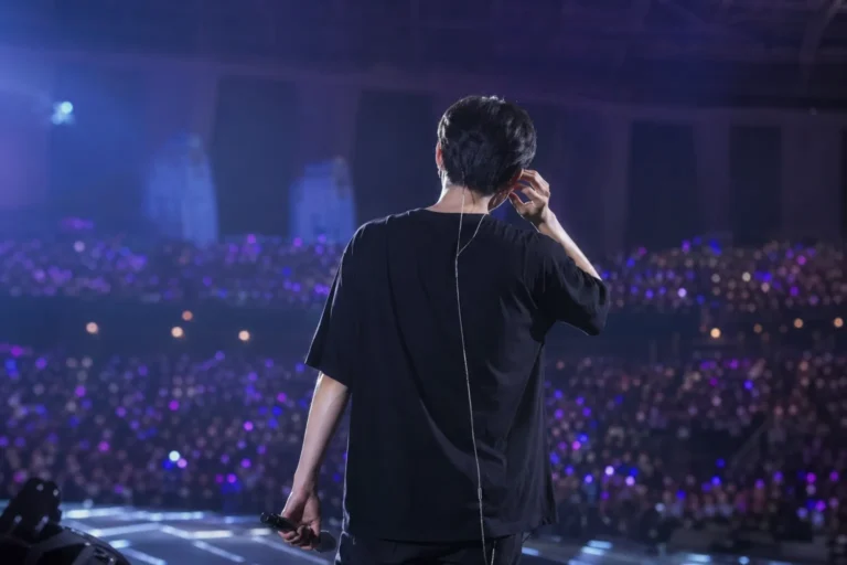 K-pop performer on stage during a sound issue with blurred arena crowd and purple lighting