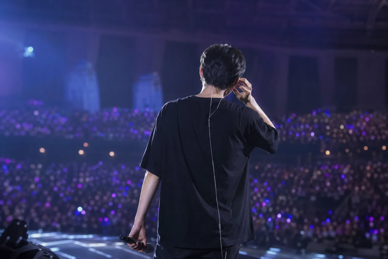 K-pop performer on stage during a sound issue with blurred arena crowd and purple lighting