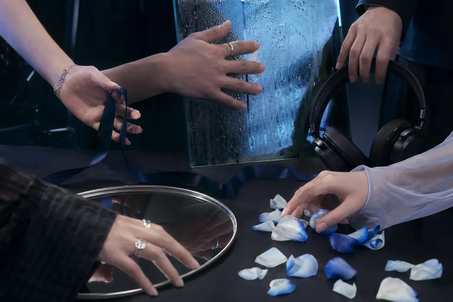 A cinematic five-senses concept scene with hands, reflective glass, silk, petals, and studio objects.