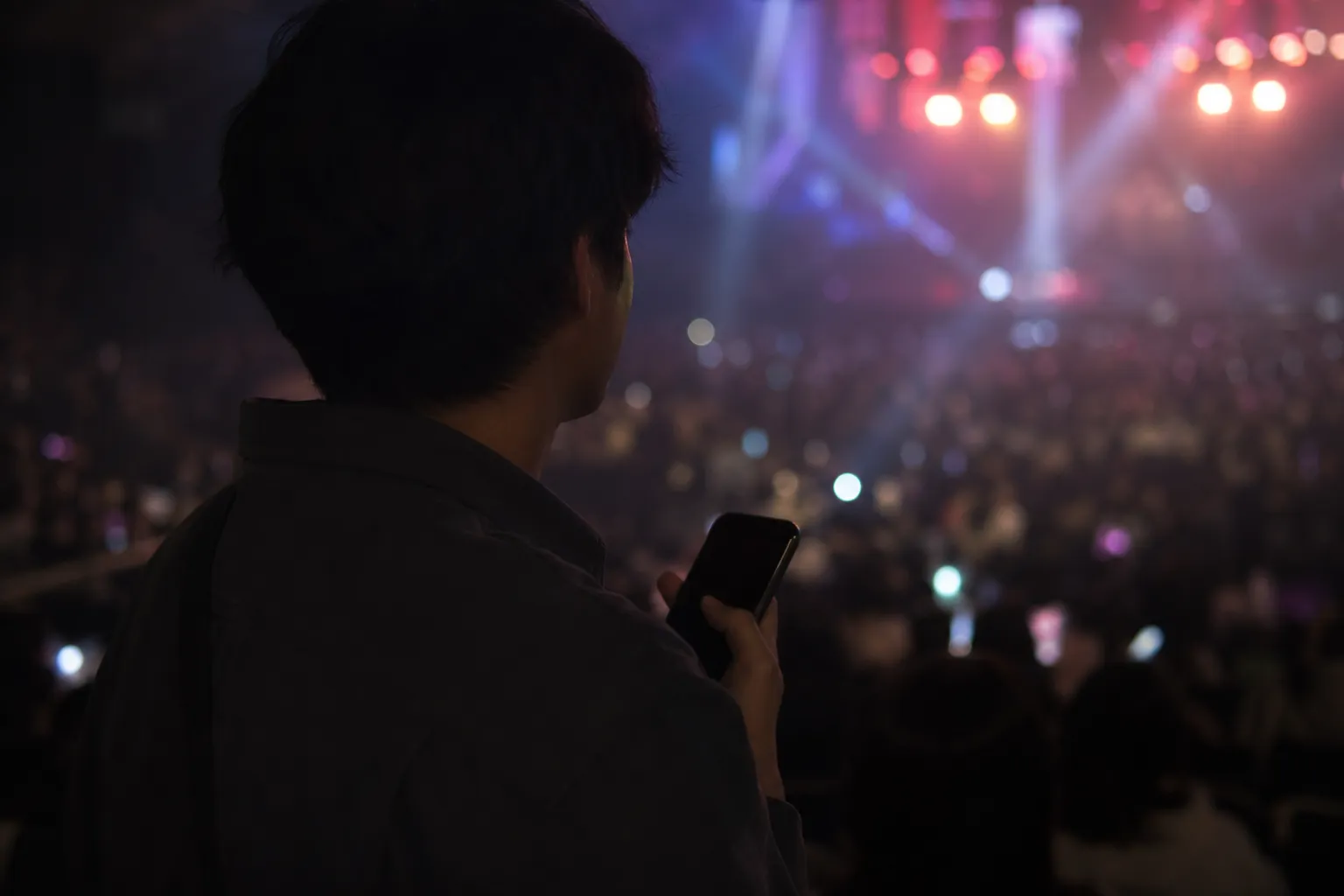 An anonymous concertgoer in a Seoul K-pop arena holding a phone while stage lights glow in the background.