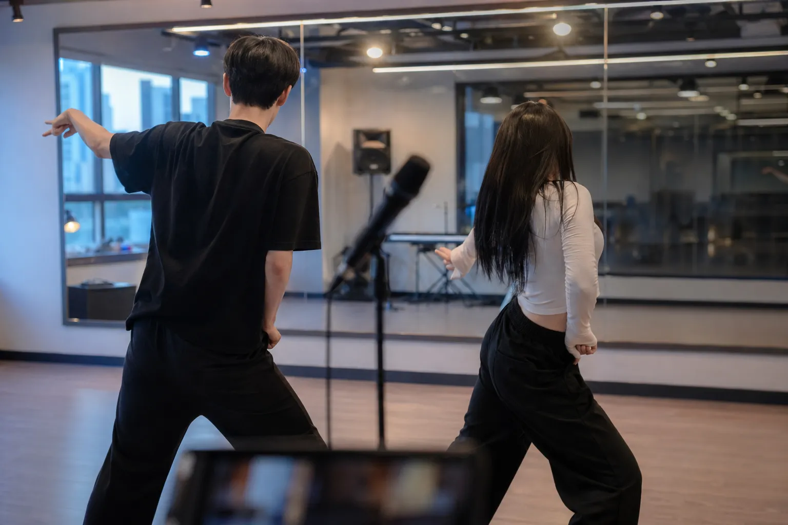 Two faceless idol trainees rehearse in a modern Seoul studio, evoking music, growth, and debut preparation.