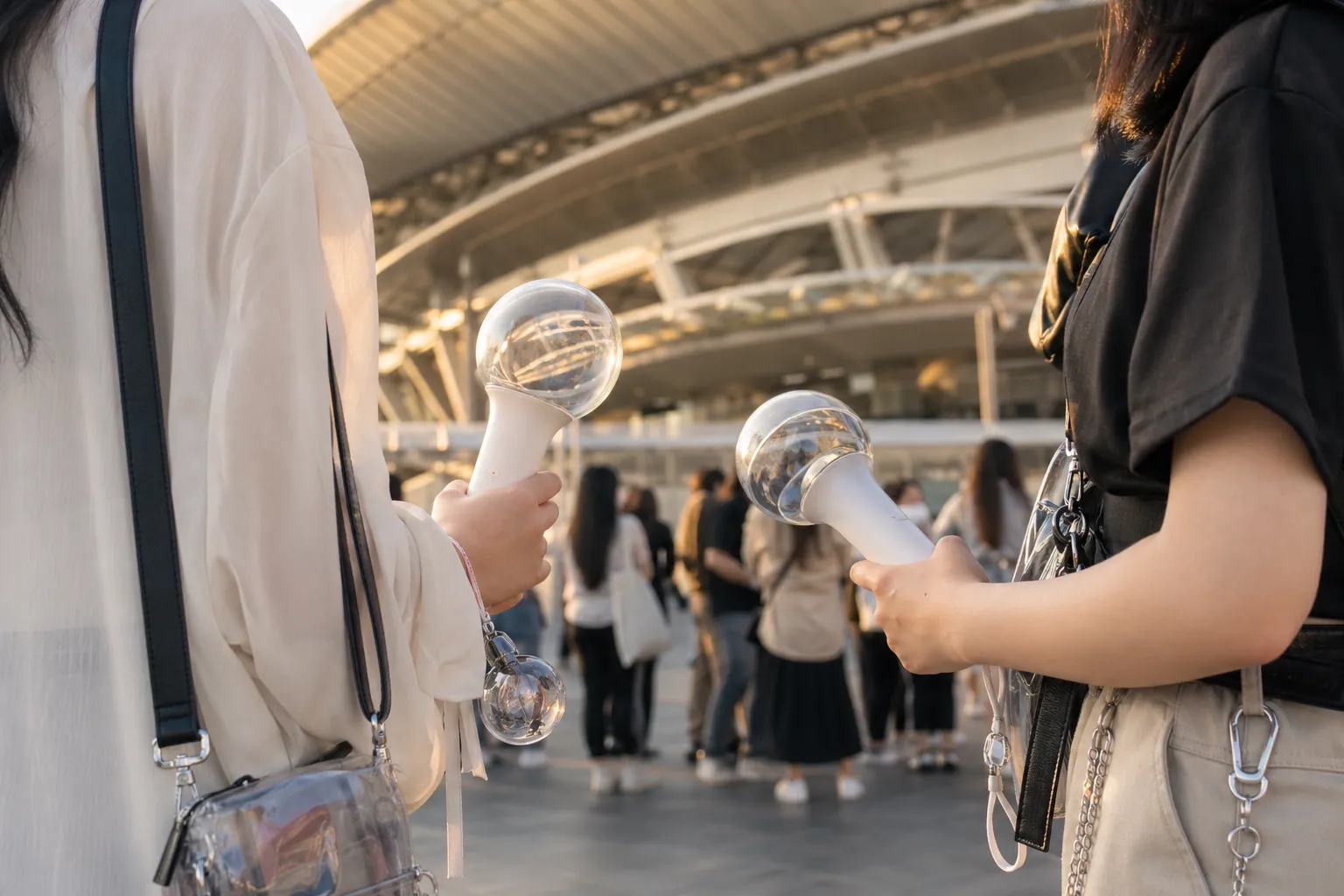 Fans with light sticks gather near a blurred stadium entrance before a major K-pop concert in Japan.