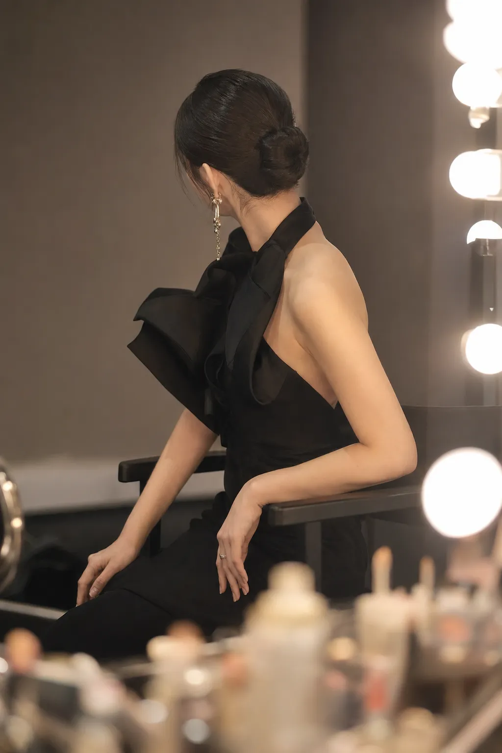 A softly obscured K-pop-inspired performer in sculptural black couture preparing backstage for a luxury gala.