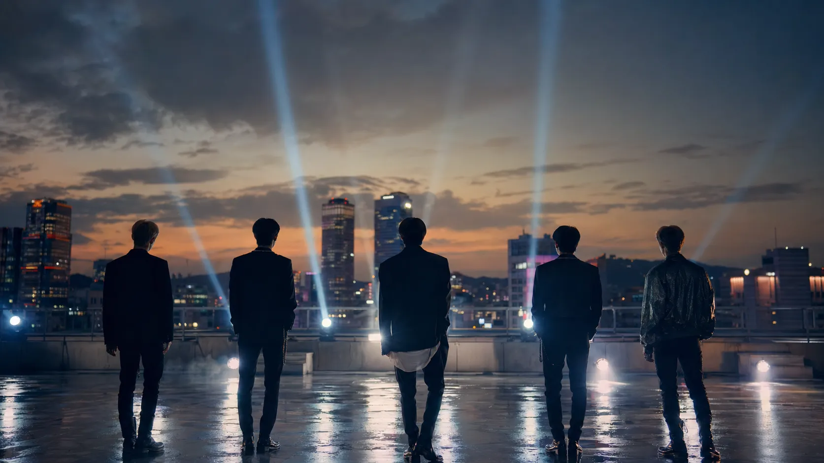 Five anonymous performers on a Seoul rooftop film set in a cinematic comeback teaser atmosphere.